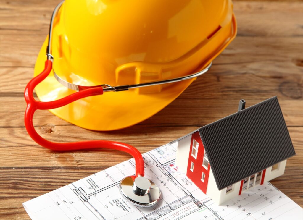 An architect’s drawing with a surveyor’s yellow hard hat with stethoscope, indicating a health check on the plans.