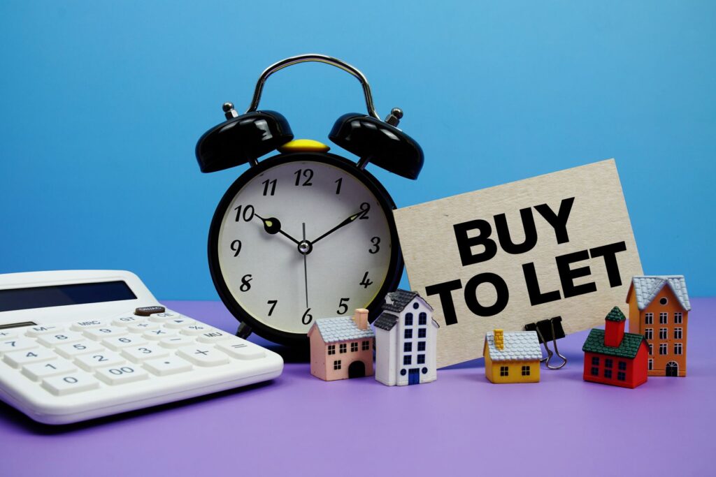 Buy to Let sign next to a calculator, alarm clock and model houses